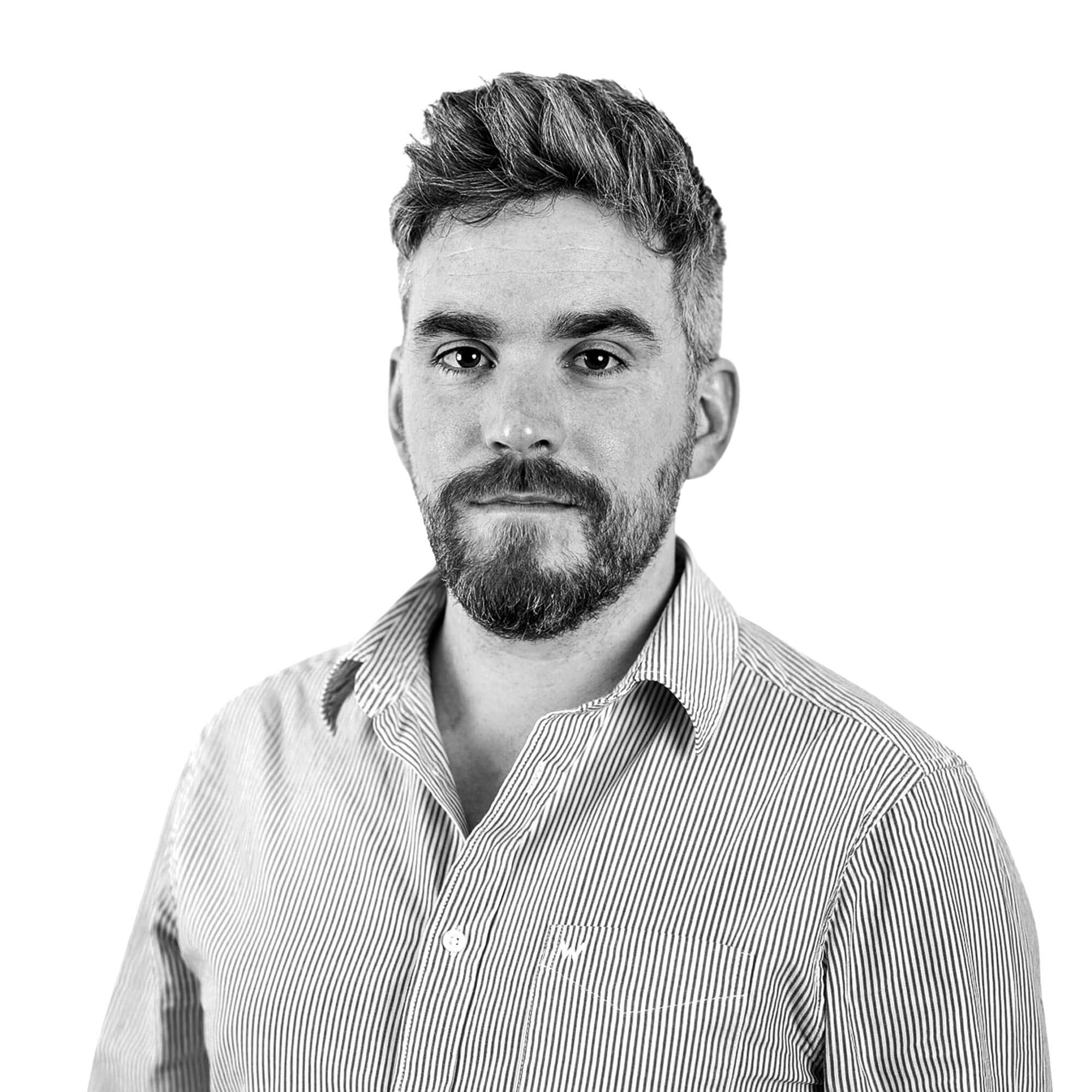 A black and white image of a man with a beard and spiked-up hair, he is wearing a button down shirt. When you hover over the image it changes to him holding his hands up to resemble a rectangle framing