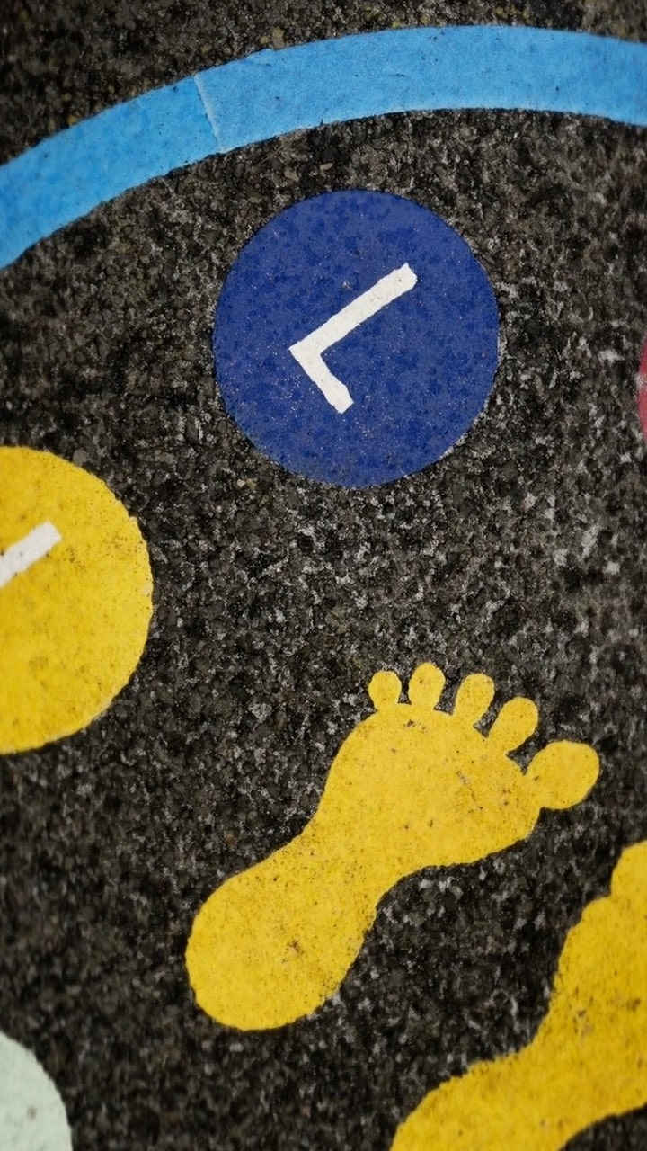 An image of concrete with yellow childrens feet painted on it, and a blue circle with a white L in it