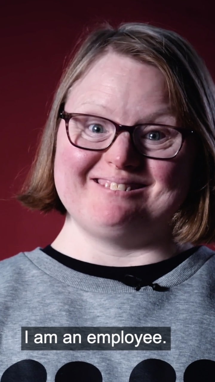 An image of a young woman with glasses smiling, she has short brown hair and a grey shirt - the subtitle says "I am an employee".