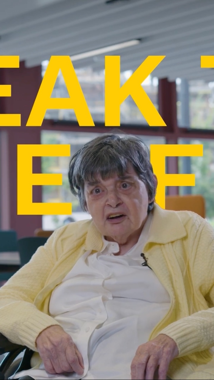 An older woman sitting in a chair. Behind her text that is cropped off is positioned floating.