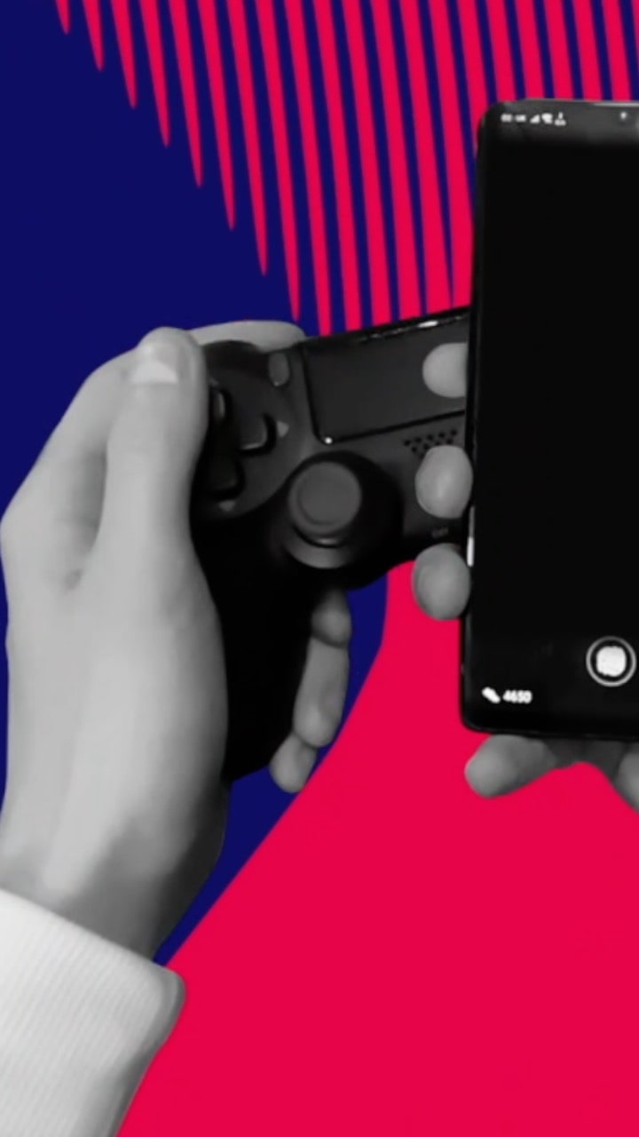 An image of a pair of grey hands holding a black gaming controller and a phone.